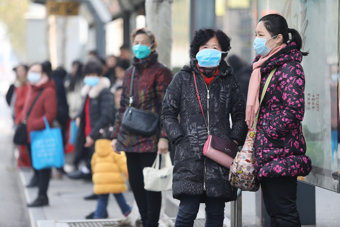 Bewoners van Wuhan wachten op de bus, vlakbij de gesloten vismarkt.