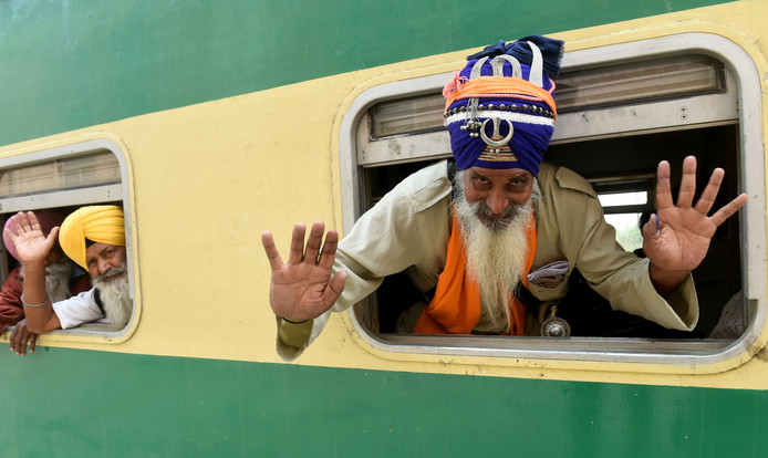 Een Sikh-pelgrim zwaait vanuit het raam van een trein als deze aankomt op het Wagah-station in Wagah, Pakistan waar de geboortedag wordt gevierd van Baba Guru Nanak. Foto Rahat Dar