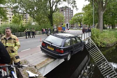 Vrouw met kinderen ramt hekwerk op brug en balanceert in auto boven de stadsgracht