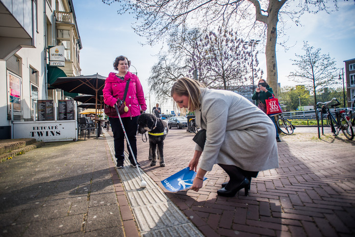 Martien Louwers plakt in aanwezigheid van Marjolein van den Broek en haar hond Harvey een sticker naast de geleidelijn